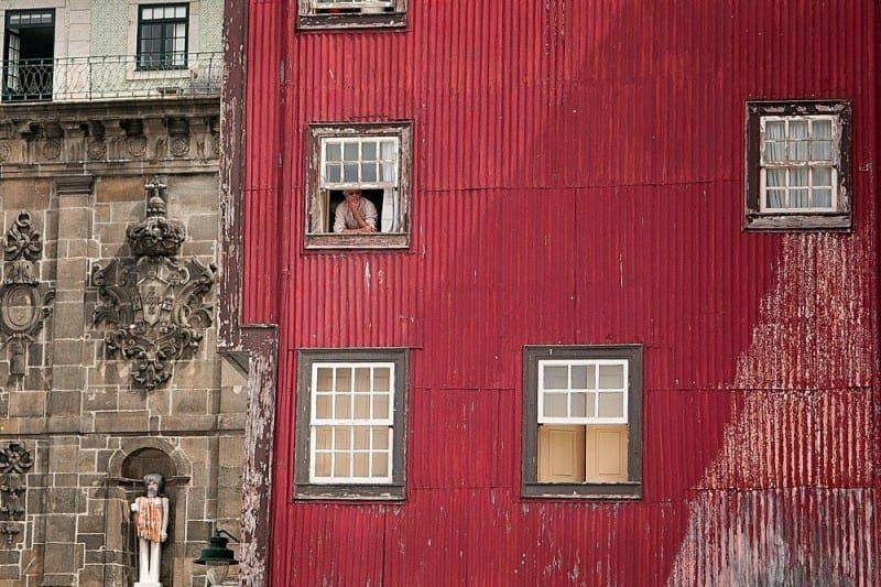 man looking out of window of red building thinking about how to travel when you're young