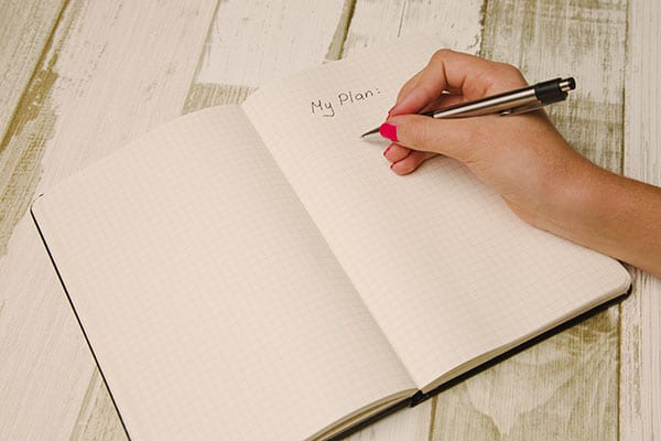 woman writing list in notebook to boot your confidence